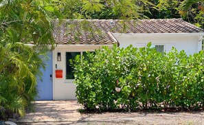 Une maison avec un toit en tuiles, une porte bleue et un petit jardin avec un feuillage verdoyant.