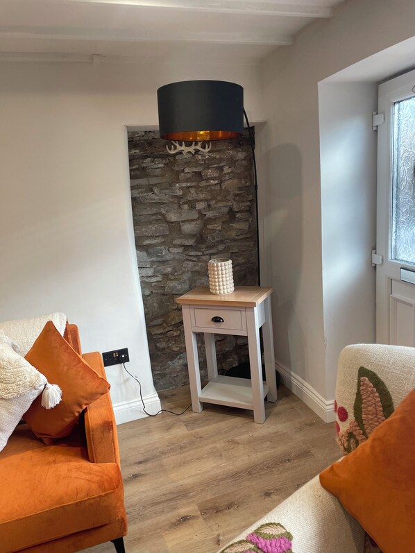 A cozy living room with a stone wall, a small wooden side table, and a modern lamp. - Charming 1-bed Cottage in Brynmenyn (Bridgend)