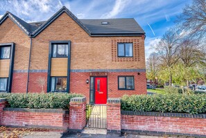 Stunning two-story residence with a brick facade and black roof, featuring a red door and black-framed window.