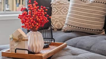 Un salón acogedor con un sofá gris, un jarrón decorativo con bayas rojas y una bandeja de madera con una tarjeta con forma de casa y una pequeña caja de regalo.