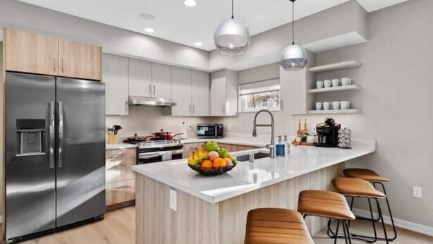 Une cuisine moderne dotée d’appareils électroménagers en acier inoxydable, d’un îlot central avec des tabourets et de meubles de rangement en bois.