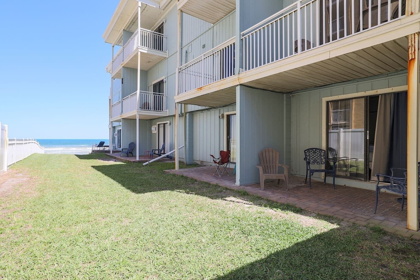 A beachfront hotel with multiple balconies, outdoor seating, and a grassy lawn.