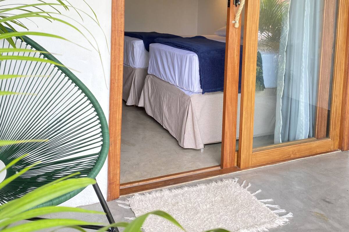 Ein Zimmer mit einem Bett, einer Holztür, einer Pendelleuchte und einer Pflanze.