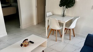 Uma sala de estar moderna, com uma mesa de centro branca, um sofá azul e um espaço de jantar com cadeiras brancas e uma pequena mesa.