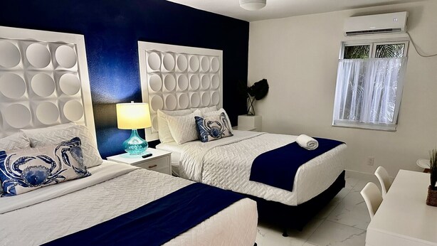 Quarto de hotel com duas camas, uma escrivaninha e uma janela com cortinas.