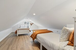 A bedroom with a sloped ceiling, a bed with patterned bedding, a small bedside table, and a window with a view.