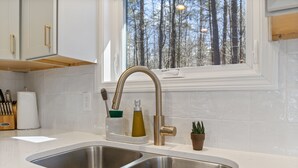 A kitchen with two stainless steel sinks, a window with a view of trees, and a countertop with a knife block and a bottle.