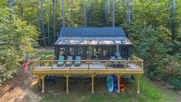 A cabin with a deck, large windows, and kayaks stored underneath.