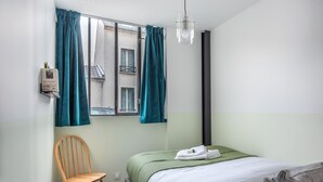 A bedroom with a bed, a chair, a window with curtains, a hanging light fixture, and a wall-mounted shelf with a book. - Hedonist House - Design Architect Flat - 15min. from Paris center (Gentilly)