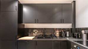 A modern kitchen with dark cabinets, a stainless steel sink, and a built-in oven. - Hedonist House - Design Architect Flat - 15min. from Paris center (Gentilly)