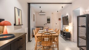 A modern dining area with a wooden table and chairs, a TV on the wall, and a bookshelf. - Hedonist House - Design Architect Flat - 15min. from Paris center (Gentilly)