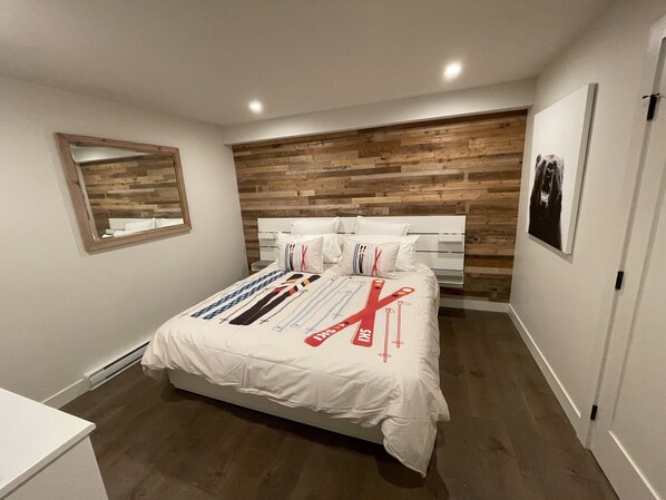 A bedroom with a wooden headboard, a bed with a white comforter, a bedside table, and a mirror on the wall.