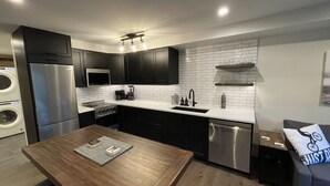 A modern kitchen with dark cabinets, a stainless steel refrigerator, a built-in oven, and a dishwasher.