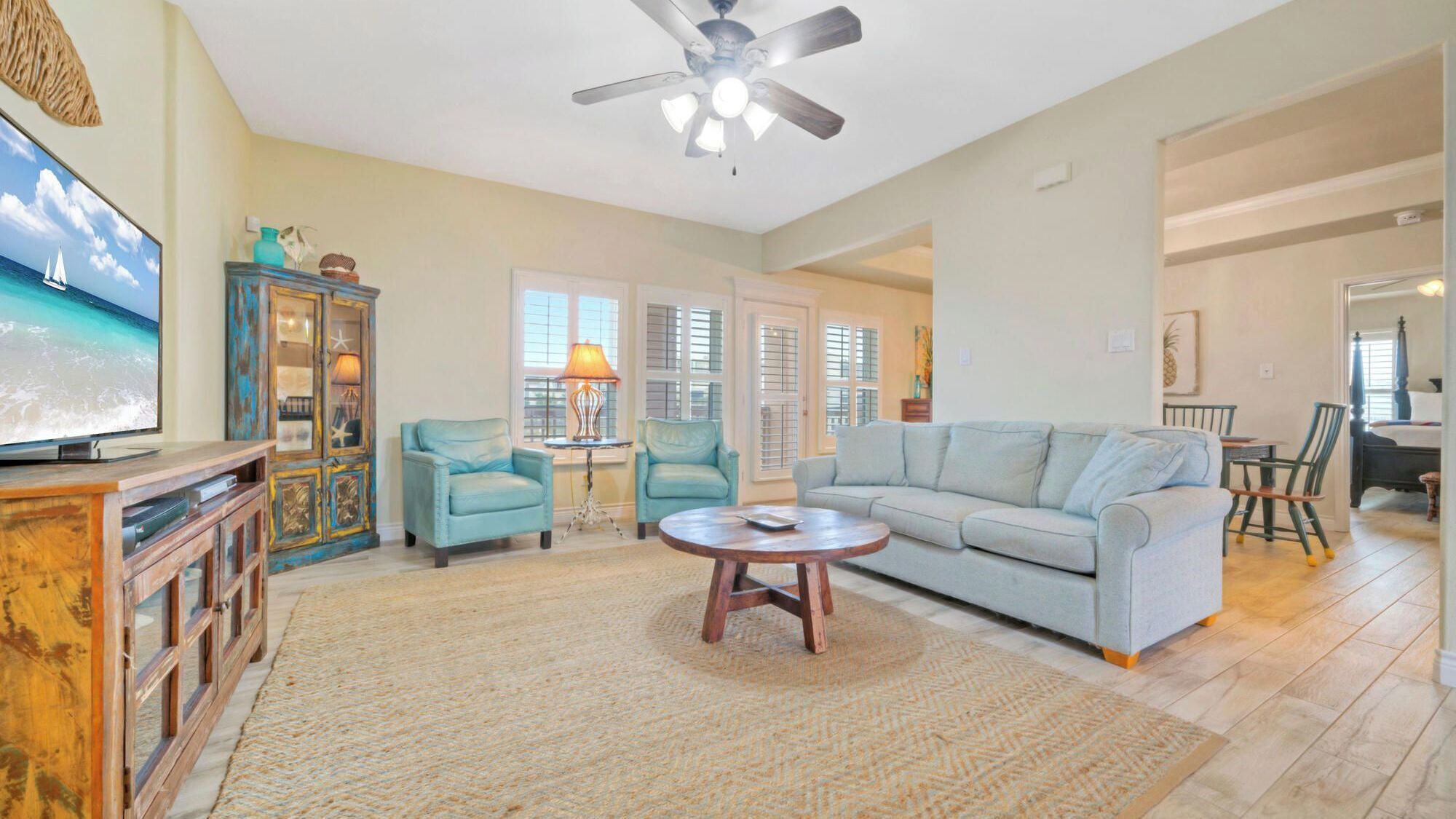 A living room with a television, a sofa, two armchairs, a coffee table, and a ceiling fan.
