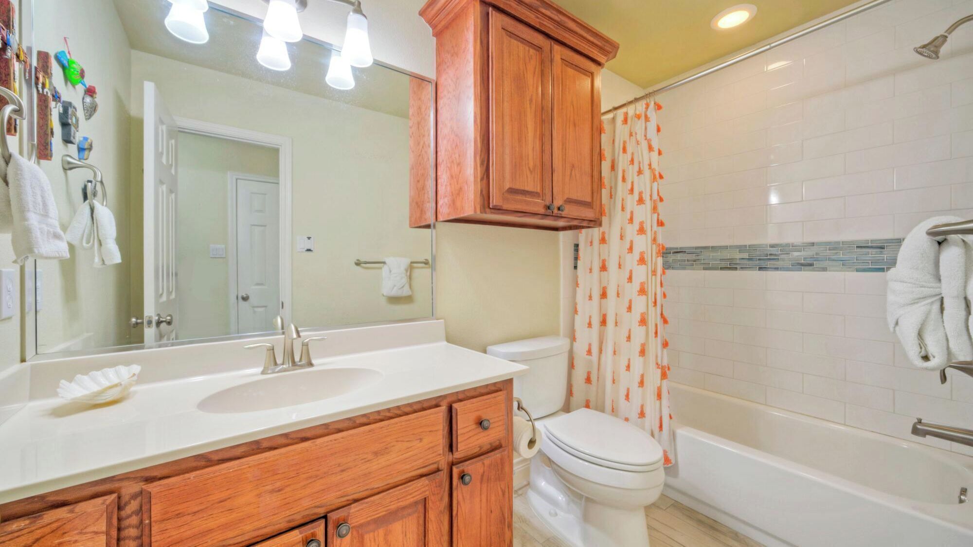Une salle de bain avec un meuble-lavabo en bois, des toilettes, une baignoire et un rideau de douche.