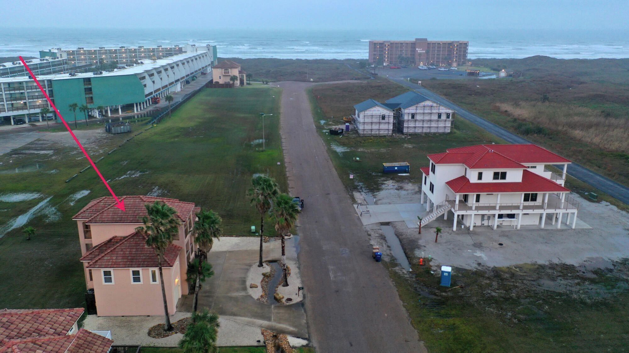 Un hotel costero con un camino largo que lleva a la playa, un estacionamiento y vista al océano.
