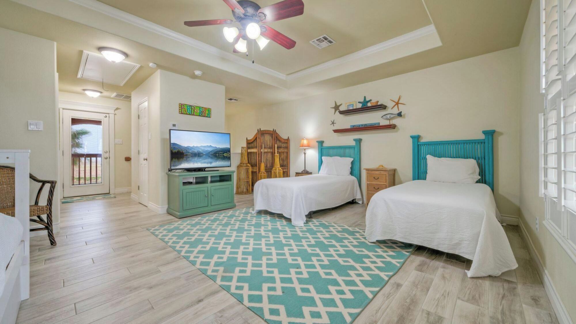 A bedroom with two beds, a TV, a ceiling fan, and a decorative wall shelf.