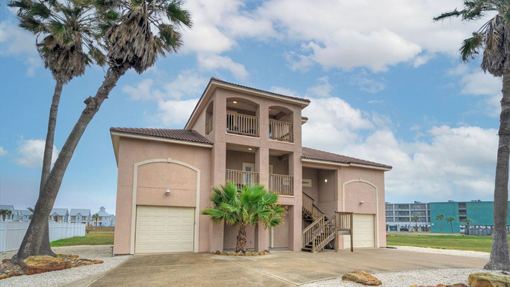 A multi-story building with a central staircase, two garage doors, and a balcony on the upper floor.