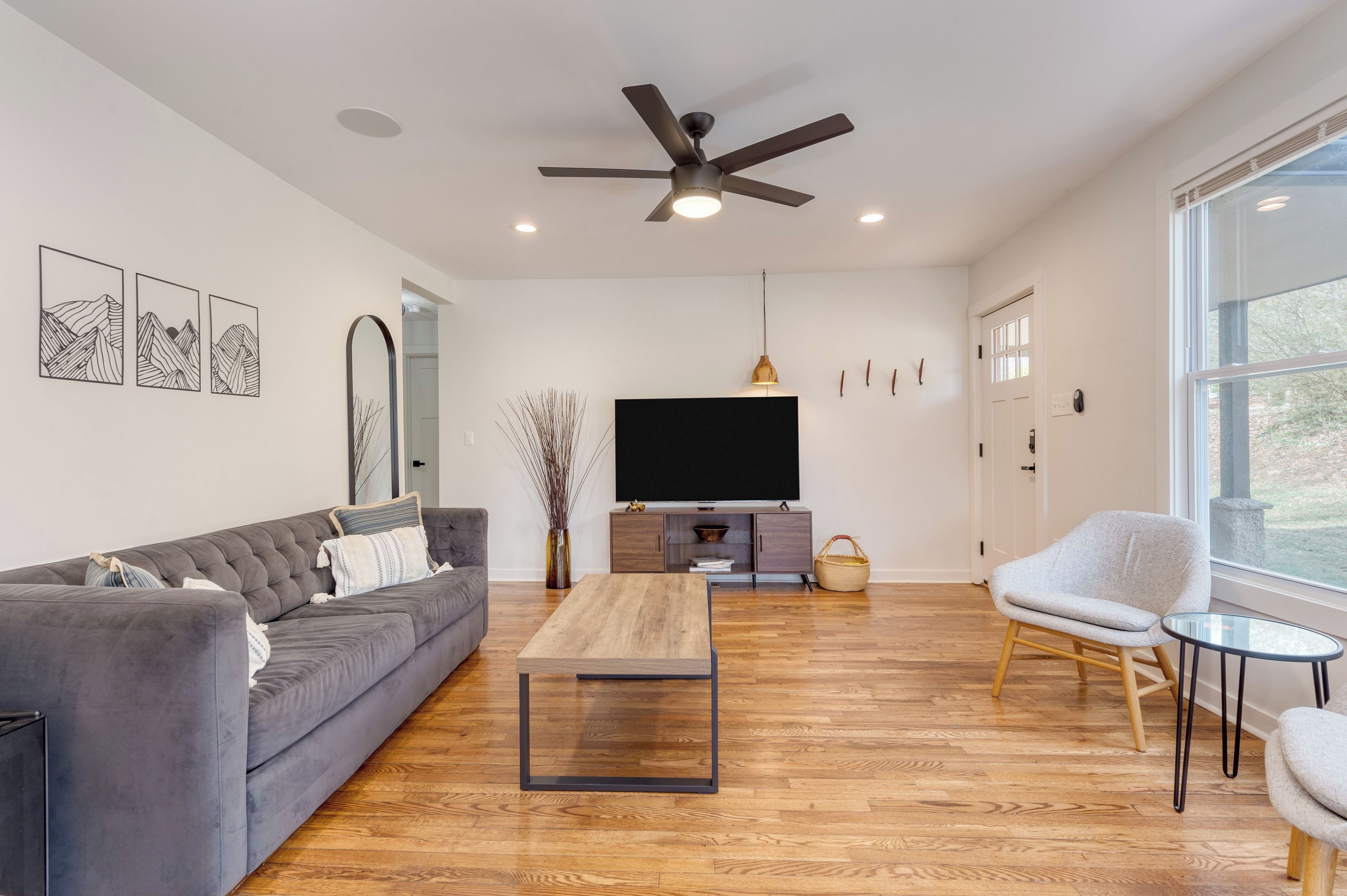 A modern living room with a grey sofa, a wooden coffee table, a grey armchair, a TV, and a ceiling fan.