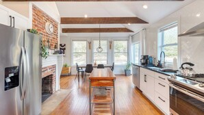 A modern kitchen with a brick fireplace, wooden beams, and large windows.