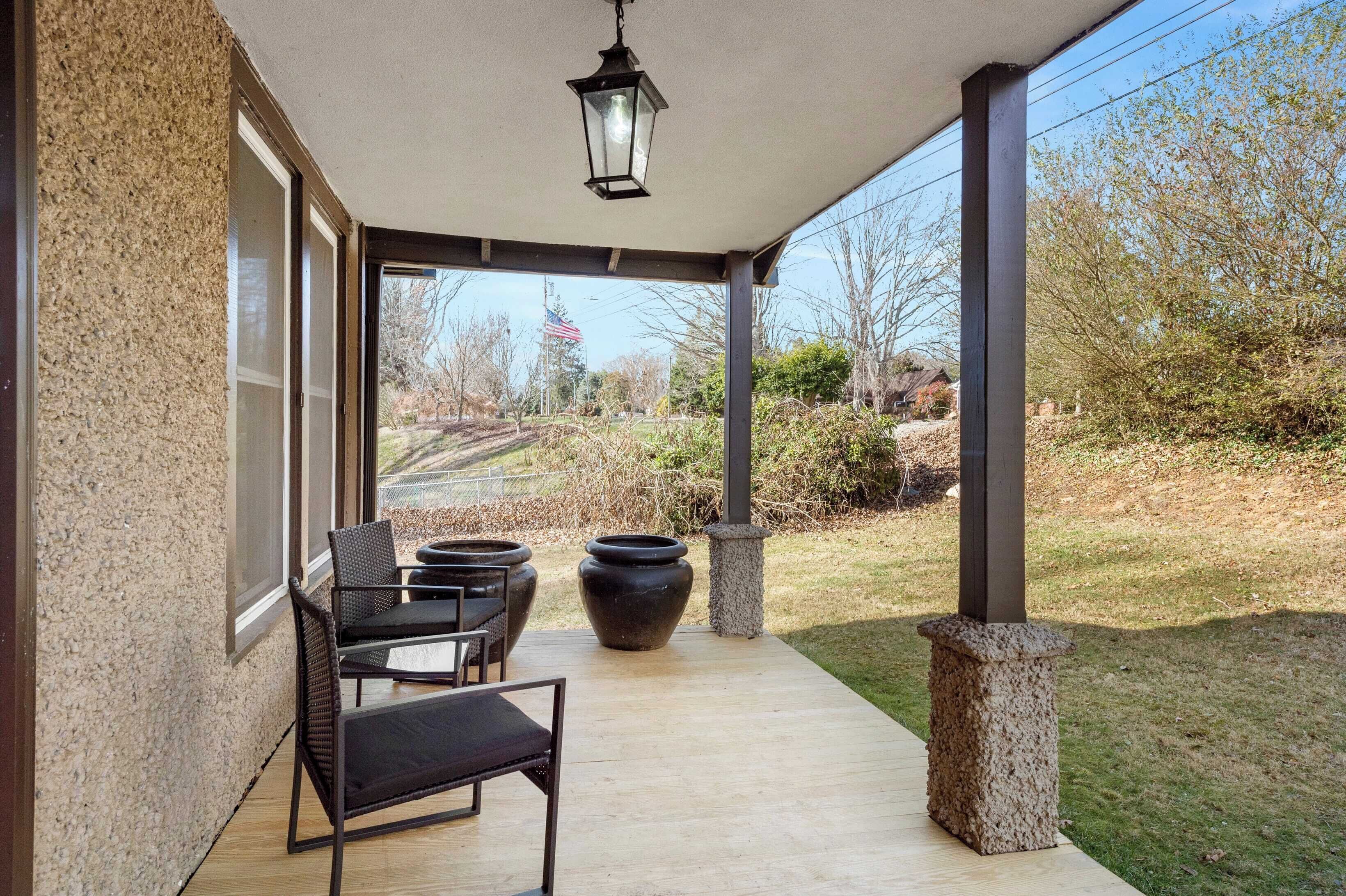 A covered patio with outdoor seating, a hanging lantern, and a view of a grassy area with trees and a flag.