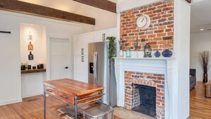 A kitchen with a brick fireplace, white cabinets, and a wooden table.