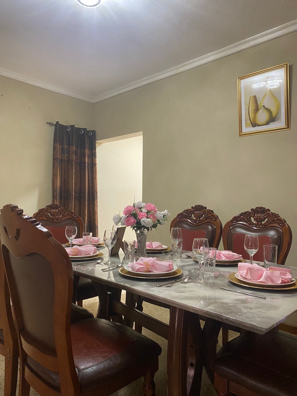 Een eetkamer met een marmeren tafel gedekt voor vier personen, met houten stoelen voorzien van gedetailleerde houtsnijwerken.