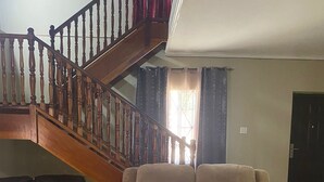 A living room with a wooden staircase, a black leather sofa, a beige recliner with cushions, and a patterned rug. - Lachemar Guest House (Ocho Rios)