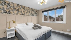 Una camera da letto con un letto, un comodino, una lampada, una finestra e una parete decorata con un motivo a foglia.