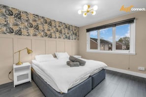 A bedroom with a bed, a nightstand, a lamp, a window, and a wall with a leaf pattern. - West Lothian 5 Beds + car space (Whitburn)