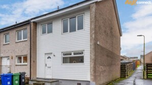 Un edificio residenziale a due piani con facciata bianca, una porta d'ingresso e un piccolo cortile anteriore.