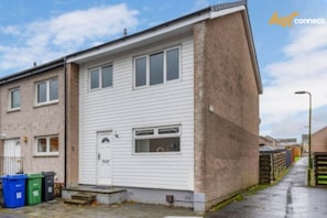 A two-story residential building with a white exterior, a front door, and a small front yard. - West Lothian 5 Beds + car space (Whitburn)