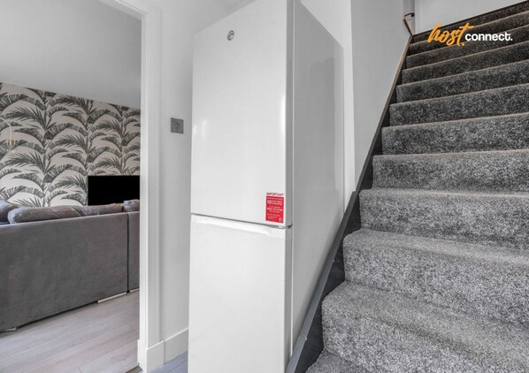 A staircase leading to a landing with a white wall and a red sign, a grey sofa, and a patterned wallpaper in the background.