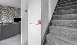 A modern living room with a grey sofa, a white refrigerator, and a staircase with grey carpet. - West Lothian 5 Beds + car space (Whitburn)