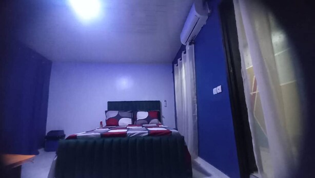 Een slaapkamer met een bed, een nachtkastje, een raam met gordijnen en een airconditioning.