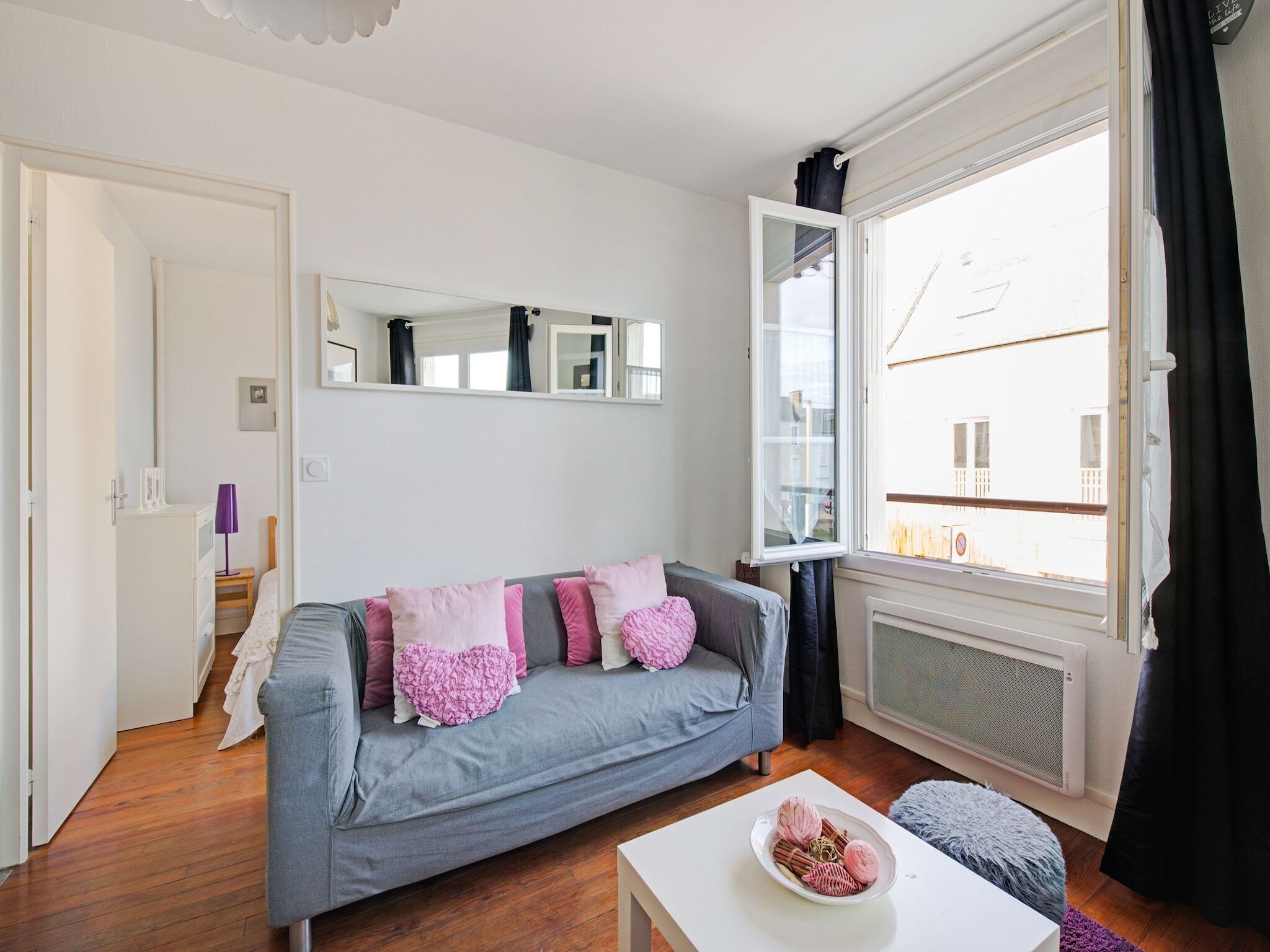 Ein modernes Wohnzimmer mit grauem Sofa, einem weißen Couchtisch und einem großen Fenster mit Blick auf Gebäude.