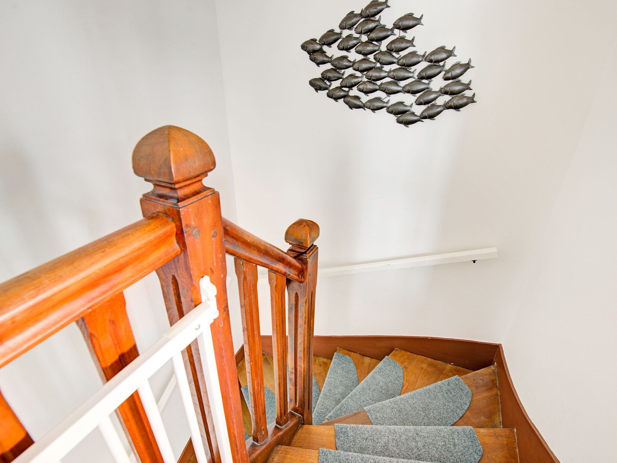 Una escalera de madera con barandilla blanca y una escultura decorativa de pez fijada a la pared.