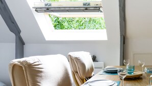 A dining area with a table set for four, a skylight above, and a view of greenery outside. - Romantic Escape in Normandy (Isigny-sur-Mer)