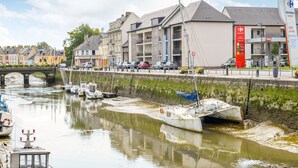A canal with boats, a bridge, and buildings including a Carrefour market. - Romantic Escape in Normandy (Isigny-sur-Mer)