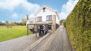A modern house with a stone facade, a covered patio, and a well-maintained lawn. - Holiday Home with Garden (Lierneux)