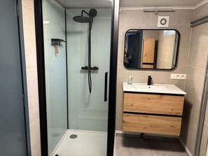 A modern bathroom with a glass-enclosed shower, a wooden vanity with a mirror, and a white sink.