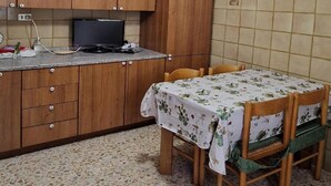 Una cocina con armarios de madera, un televisor, una mesa con mantel floral y una silla con cojín verde.