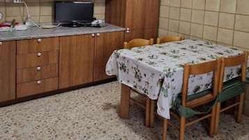 Una cucina con mobili in legno, un televisore, un tavolo con tovaglia floreale e una sedia con cuscino verde.