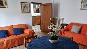 Una habitación con dos sofás naranjas, una mesa redonda con mantel azul y una planta en maceta.