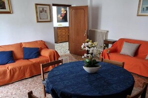 Une pièce avec deux canapés orange, une table ronde recouverte d’une nappe bleue et une plante en pot.