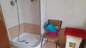 Un baño con ducha, una silla y un cubo de basura.