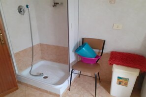 Une salle de bain avec une douche, une chaise et une poubelle.