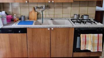 Una cucina con mobili in legno, un lavello a due vasche, un fornello a gas e una lavastoviglie.