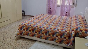 Un dormitorio con cama, una silla, cómoda y ventana con cortinas.