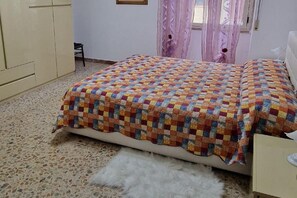 Une chambre à coucher avec un lit, une chaise, une commode et une fenêtre avec des rideaux.